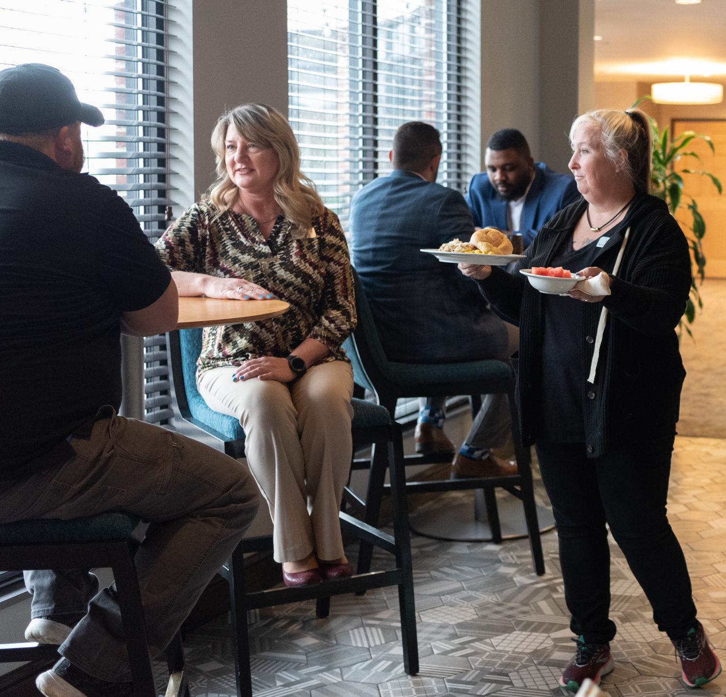 Waitress serving guests in busy restaurant with help of food service robot